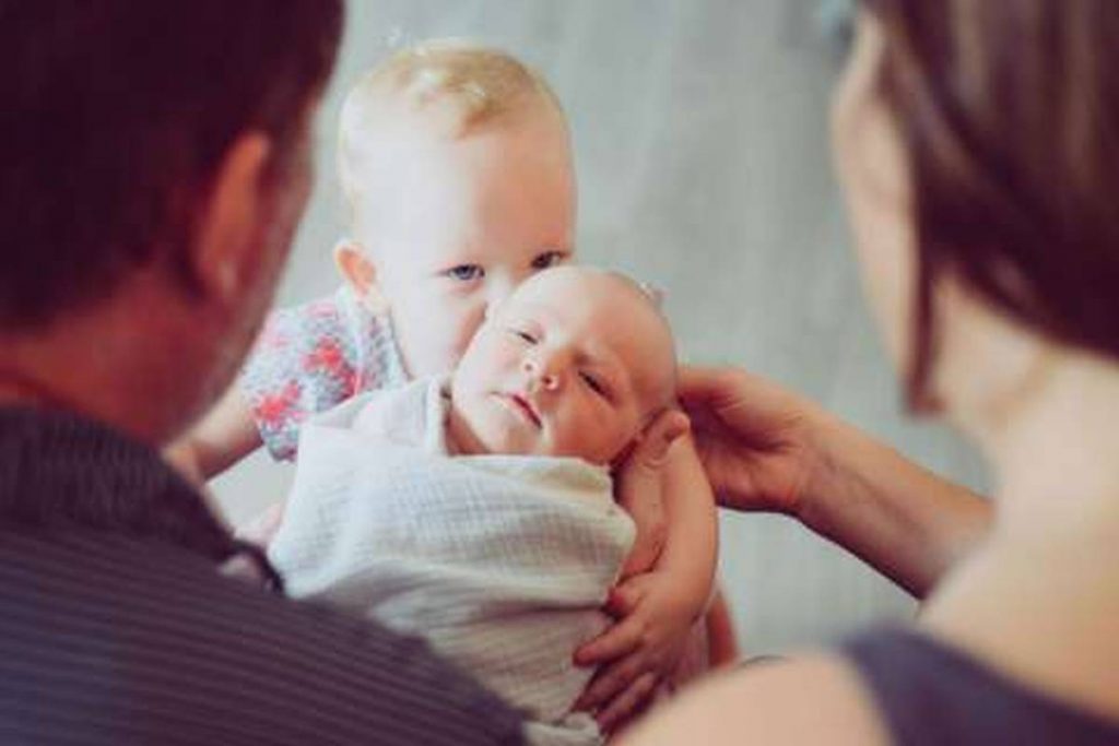 parents holding newborn with toddler