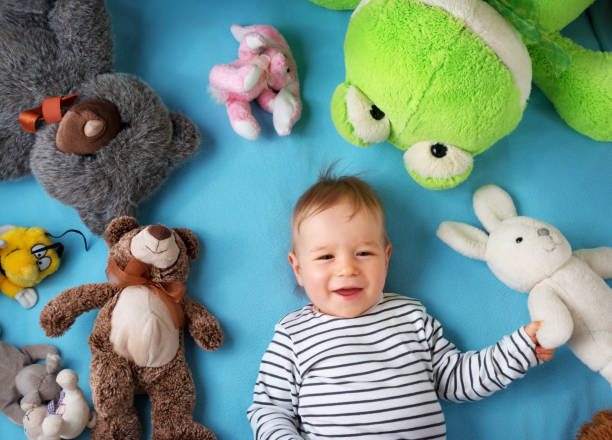 happy one year old boy lying with many plush toys on blue blanket