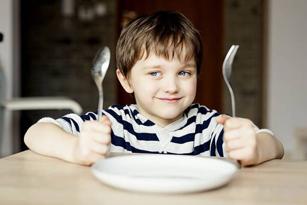happy little boy waiting for dinner. holding a spoon and fork in the hand
