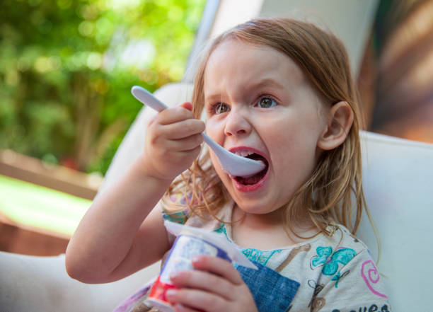 little girl eating yogurt with a big white spoon at home